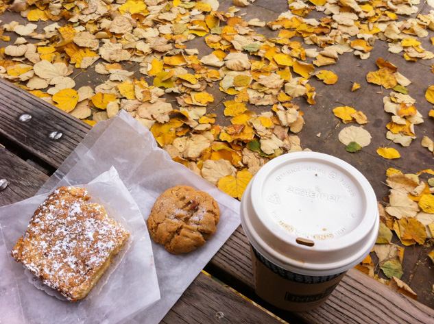 Coffee and pastry on a bench surrounded by autumn leaves in New York City